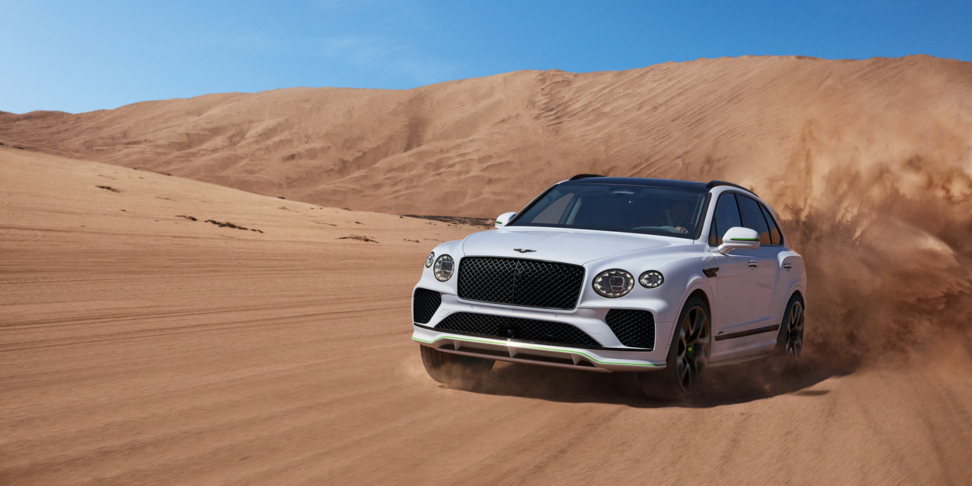 Bentley Abu Dhabi Bentley Bentayga Speed SUV front three quarter in Snow Quarts Pearlescent by Mulliner white paint driving dynamically through the desert