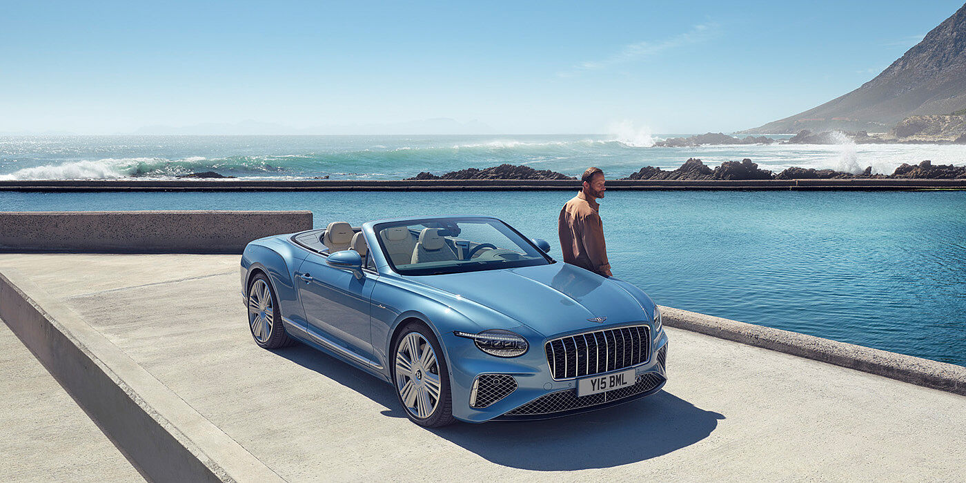 Bentley Abu Dhabi New Bentley Continental GTC Azure convertible front view in Light Windsor blue paint with 22 inch ten spoke wheels parked by the sea in the sunshine
