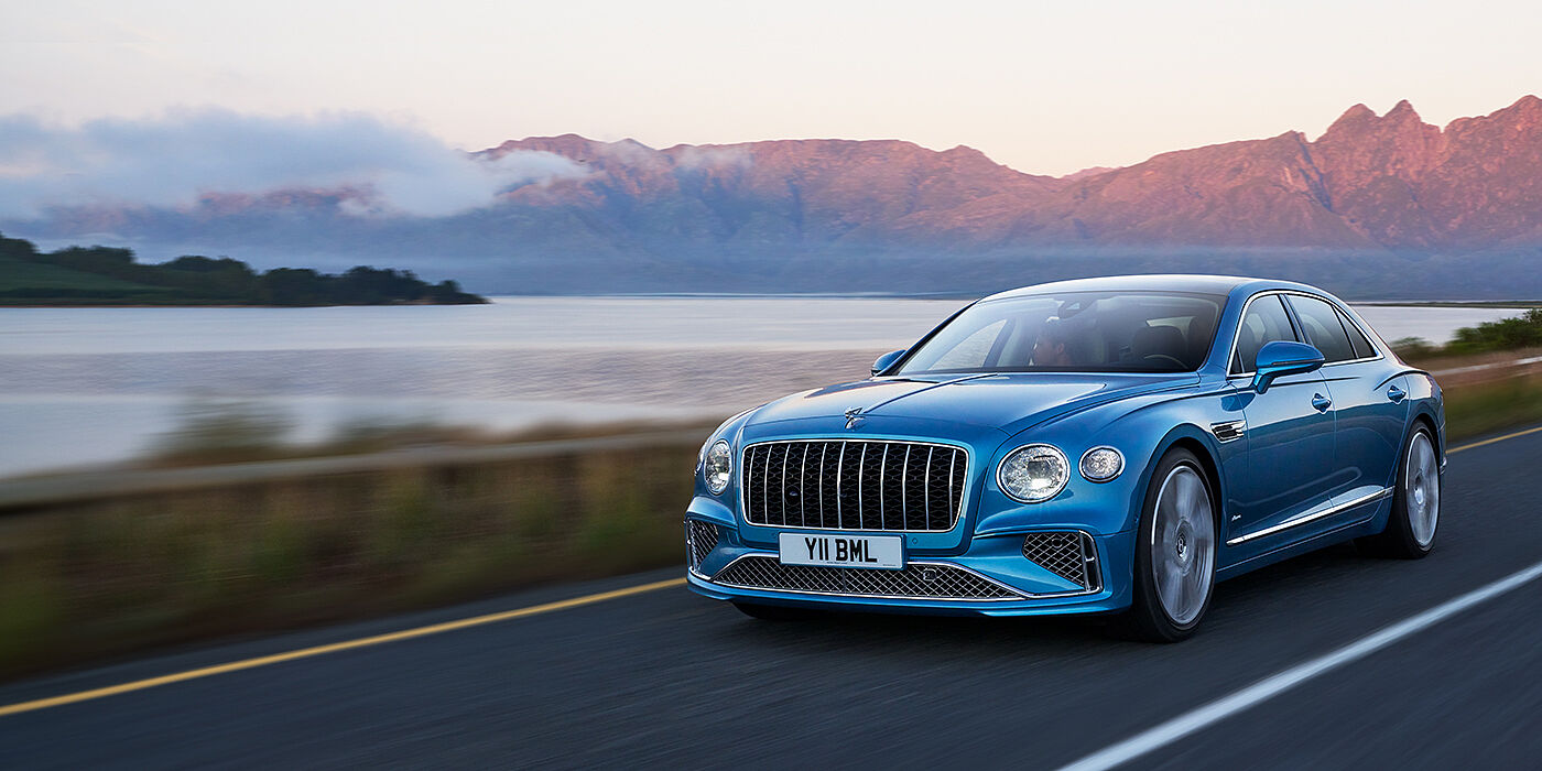 Bentley Abu Dhabi New Bentley Flying Spur Azure sedan in Light windsor blue paint by Mulliner, with 22 inch Azure wheels and chrome straight vaned grille driving on a mountain road