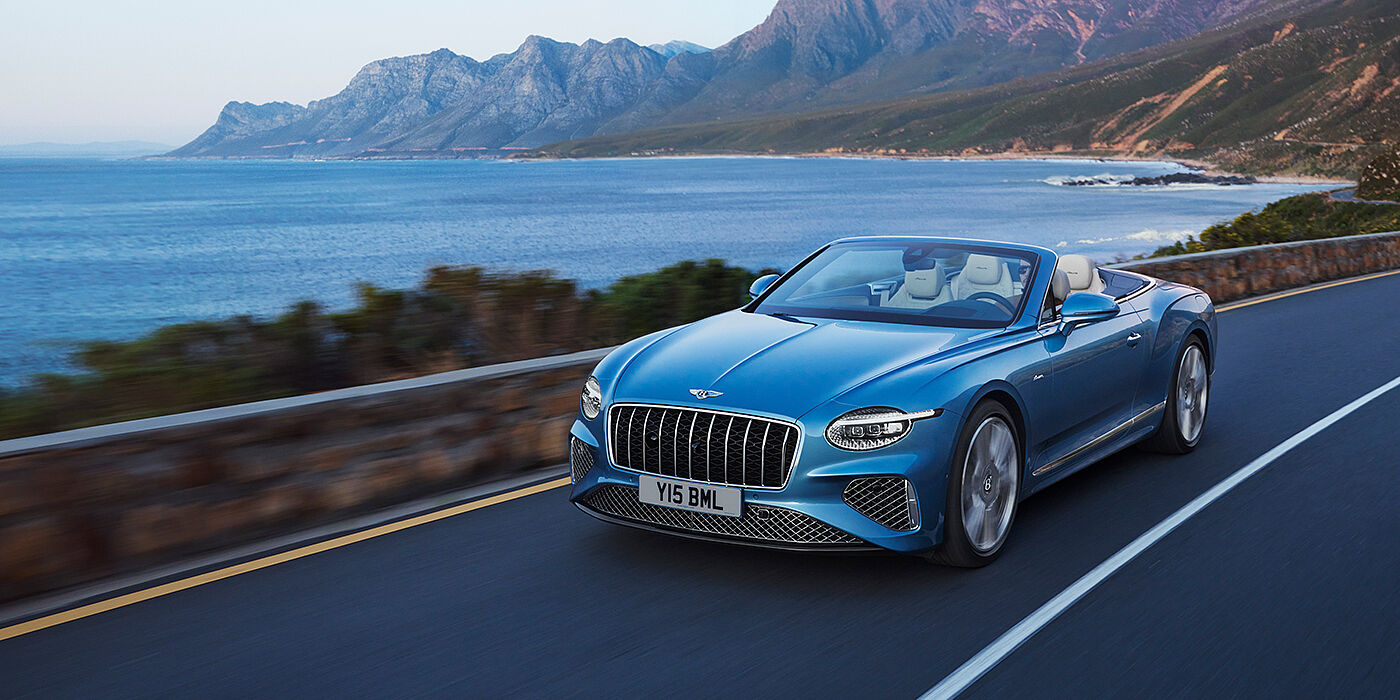 Bentley Abu Dhabi New Bentley Continental GTC Azure convertible in Light Windsor blue paint with 22 inch Azure wheels and chrome grill, driving dynamically by the sea