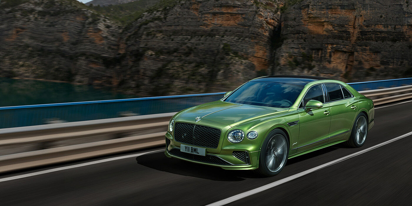 Bentley Abu Dhabi Bentley New Flying Spur Speed v8 hybrid sedan driving dynamically on a mountain road in Tourmaline Green paint