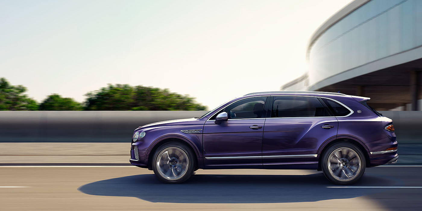 Bentley Abu Dhabi Bentley Bentayga Extended Wheelbase Mulliner luxury SUV profile in Tanzanite Purple paint, driving on an country road past trees.