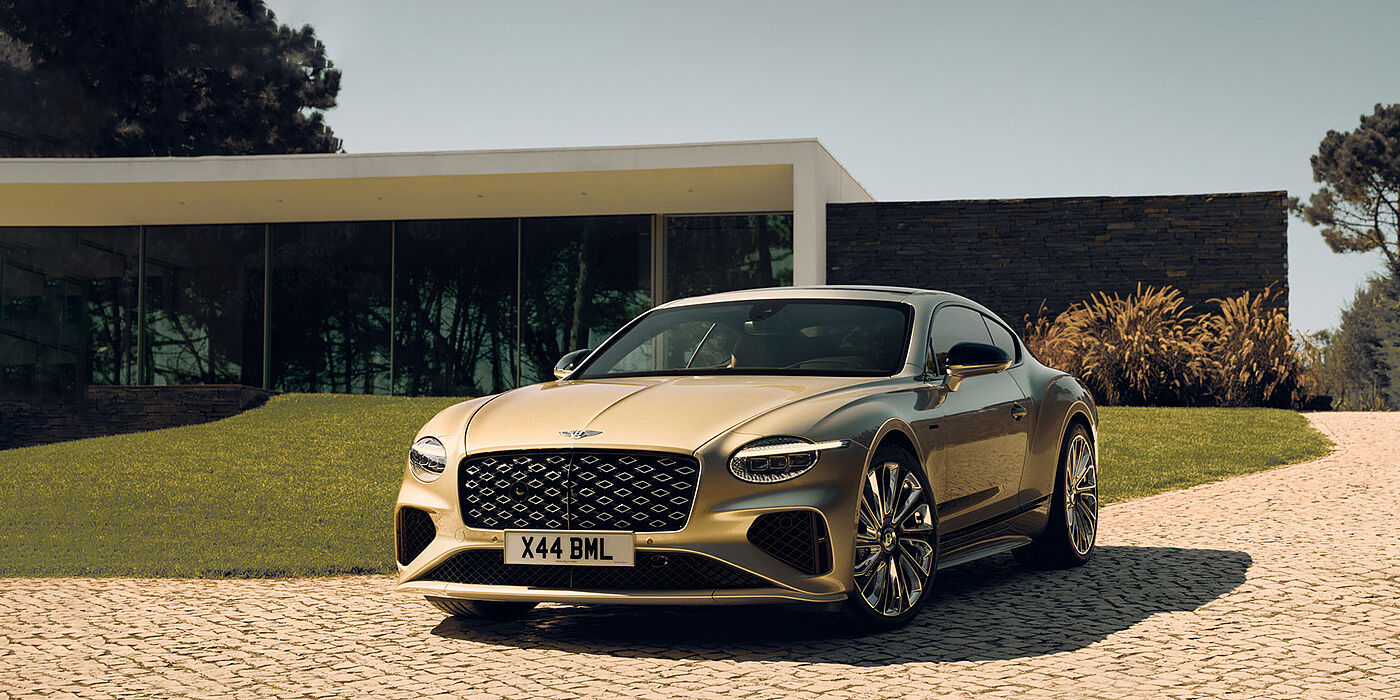 Bentley Abu Dhabi Bentley Continental GT Mulliner coupe front three quarters in Patina paint parked outside a glass fronted building with a grass lawn behind it