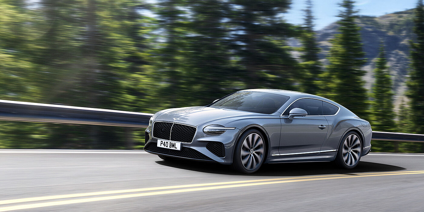 Bentley Abu Dhabi New Bentley Continental GT coupe in Silverlake paint and 22 inch ten-spoke wheels, driving dynamically on a tree-lined road in the sunshine