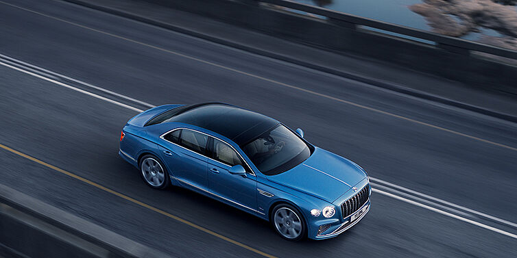 Bentley Abu Dhabi New Bentley Flying Spur Azure sedan in Light windsor blue paint by Mulliner, with 22 inch Azure wheels seen from overhead driving dynamically on a country road