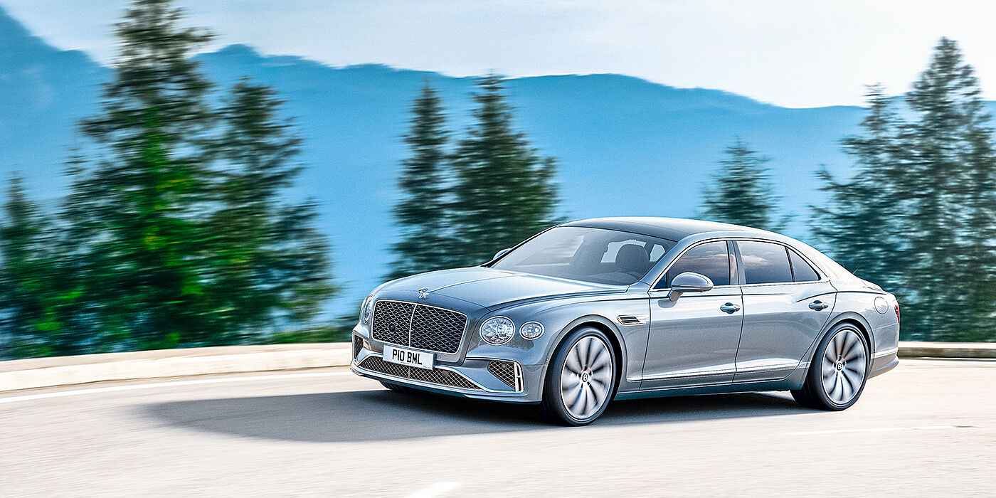 Bentley Abu Dhabi New Bentley Flying Spur sedan side view in Silverlake paint with ten spoke wheels and chrome matrix grille driving dynamically on a mountain road