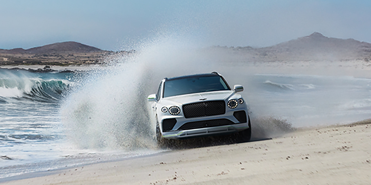 Bentley Abu Dhabi Bentley Bentayga Speed SUV facing front in Snow Quarts Pearlescent white paint driving dynamically on beach