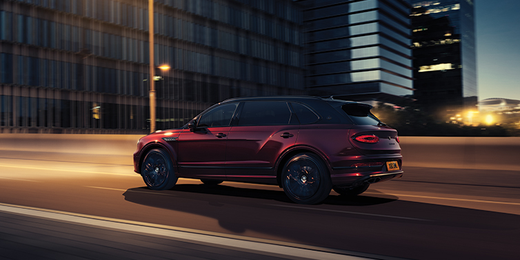 Bentley Abu Dhabi Bentley Bentayga Extended Wheelbase Mulliner SUV in Cricket Ball red paint driving dynamically in city at night